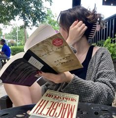 a woman sitting at a table with books in front of her and covering her eyes