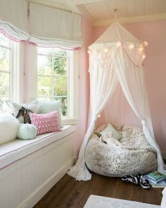 a white canopy bed in a pink room with pillows on the floor and lights hanging from the ceiling