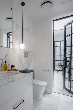 a white bathroom with marble counter tops and floor to ceiling glass doors that lead out onto an outdoor patio