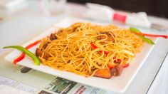 a white plate topped with spaghetti and peppers on top of a table next to a glass of water