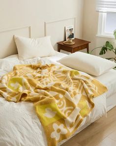 an unmade bed with yellow and white blankets on it, next to a potted plant