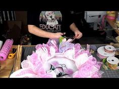 a man is making a pink and white flower out of yarns on a table