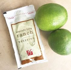 two limes sitting next to each other on top of a wooden table with a packet of ranch dressing