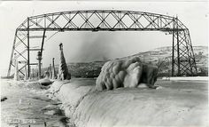 an old black and white photo of a bridge over water with ice on the ground