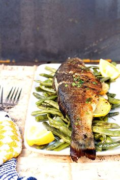 a fish is on a plate with green beans and lemons