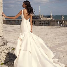 a woman in a wedding dress leaning against a stone wall looking at the ocean and sky