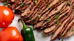 sliced flank steak with tomatoes and green peppers on the side, ready to be served