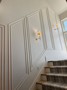 the stairs are lined with white paneling and light fixtures on either side of them