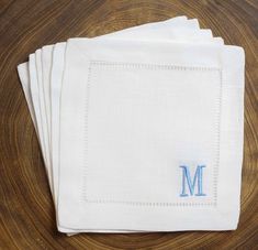 four white napkins with blue embroidered monogram on them sitting on top of a wooden table