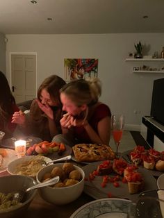 three women sitting at a table with food and drinks in front of them while one woman looks on