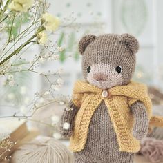 a knitted teddy bear with a scarf around it's neck sitting next to balls of yarn