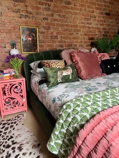 a bed with pink and green comforter next to a brick wall in a bedroom