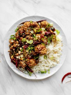 a white plate topped with rice and meat next to red chili peppers on a marble table