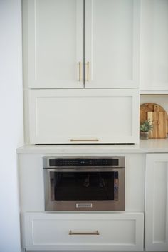 an oven built into the wall in a kitchen with white cupboards and drawers on either side