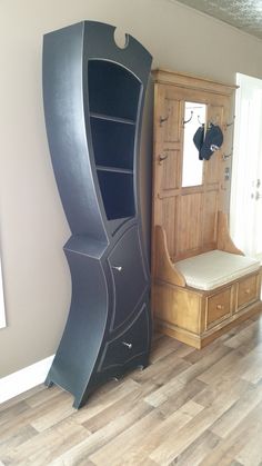 an empty room with a large black cabinet next to a wooden bench and mirror on the wall