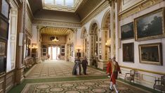 people are walking through an ornate hallway with paintings on the walls