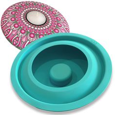 a blue and pink bowl with a candle in it next to a box that has a teal lid