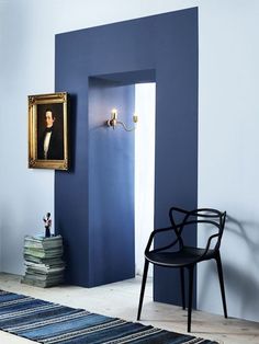 a room with blue walls and a painting on the wall next to a black chair