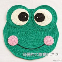 a crocheted green frog with big eyes and pink cheeks is shown in front of a white background