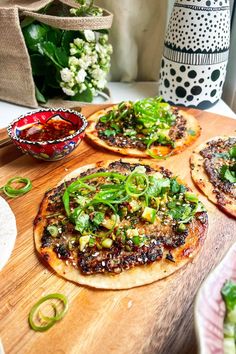 three small pizzas sitting on top of a wooden cutting board next to a vase