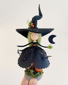 a hand holding a small doll wearing a witches hat and black dress with green hair