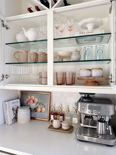 a kitchen with white cabinets and glass shelves filled with dishes, cups, and other items