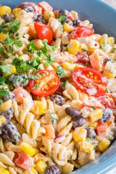 a blue bowl filled with pasta salad topped with tomatoes and black olives, parsley