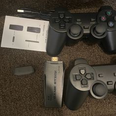 two video game controllers sitting next to each other on the floor near a charger