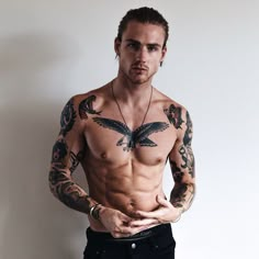 a shirtless man with tattoos on his arms and chest standing in front of a white wall