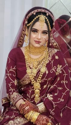 a woman in a red and gold bridal outfit sitting down with her hands on her hips