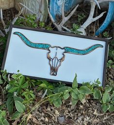 a blue and white sign with a cow skull on it's side in the grass