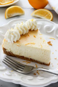 a slice of cheesecake on a plate with a fork and oranges in the background