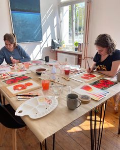 two women sitting at a table painting with watercolors