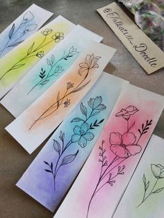 four cards with flowers painted on them sitting on a table next to some paintbrushes