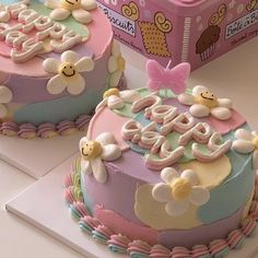 two decorated cakes sitting on top of a white table next to a pink and blue box