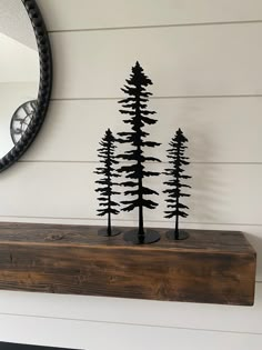 a mirror and some black trees on a shelf in front of a white painted wall