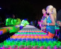 two women standing next to each other in front of many cups with neon colors on them