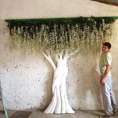 a man standing in front of a fake tree with white flowers growing out of it