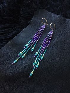 purple and green beaded earrings with gold hooks on black furnishing, close up