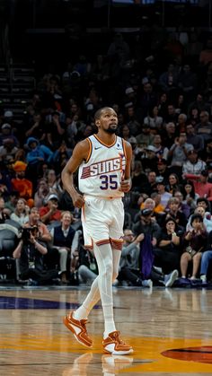 a basketball player is walking on the court in front of an arena full of people