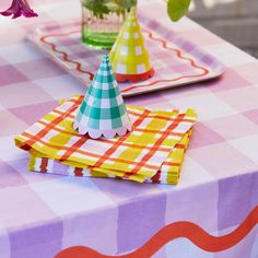 a table topped with plates and napkins covered in colorful paper hats next to flowers