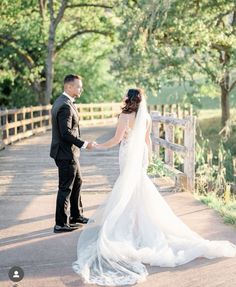 a bride and groom standing on a bridge holding hands