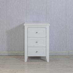 a white nightstand with three drawers against a wall