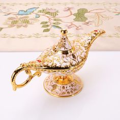 an ornately decorated teapot on a stand with gold trimmings and flowers