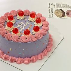 a birthday cake with pink frosting and cherries on the top is sitting on a table