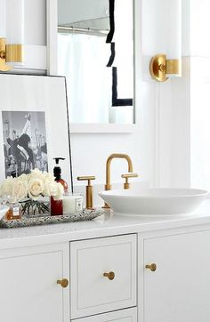 a white bathroom with gold faucet, sink and large mirror over the vanity