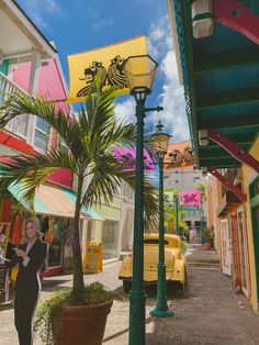 a woman standing on the sidewalk next to a palm tree in front of colorful buildings