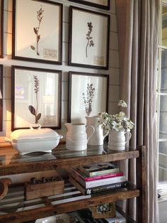 a shelf with vases and pictures on it in front of a window filled with books