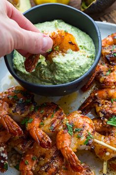 someone dipping some shrimp on skewers with guacamole