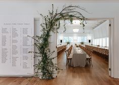 a long table set up for an event with greenery on the wall and seating